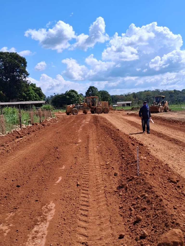 Equipe técnica acompanhando terraplanagem com motoniveladora e estacas de marcação em obra de abertura de via