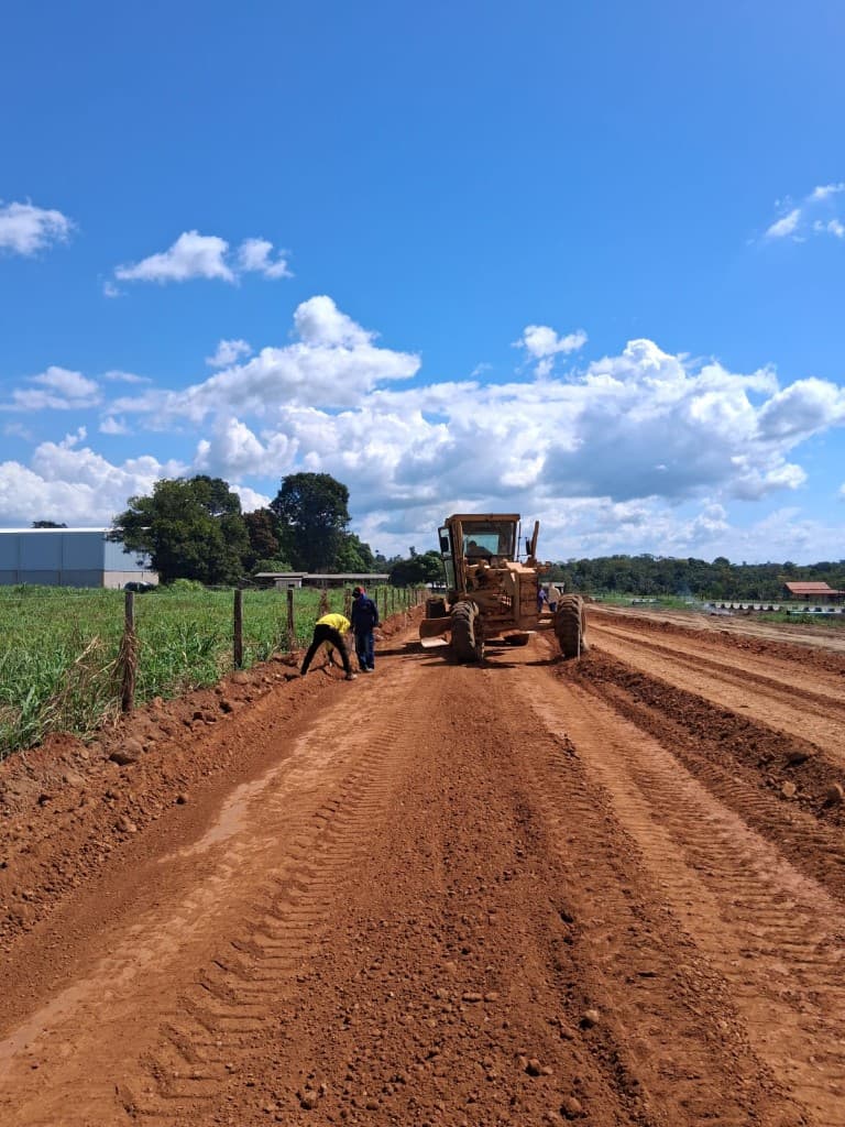 Obra de terraplanagem com motoniveladora e equipe de topografia em campo sob céu azul